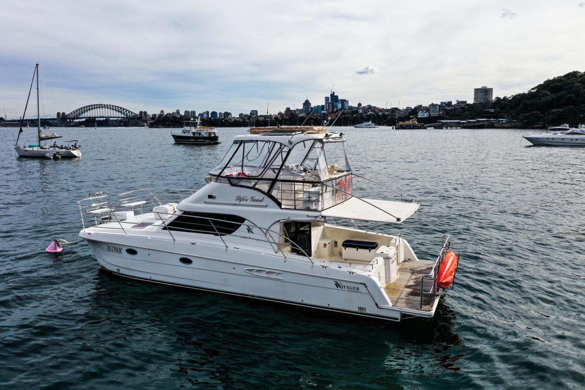 A private yacht charter named "Life's Good" floats on water with a cityscape and the Sydney Harbour Bridge in the background.