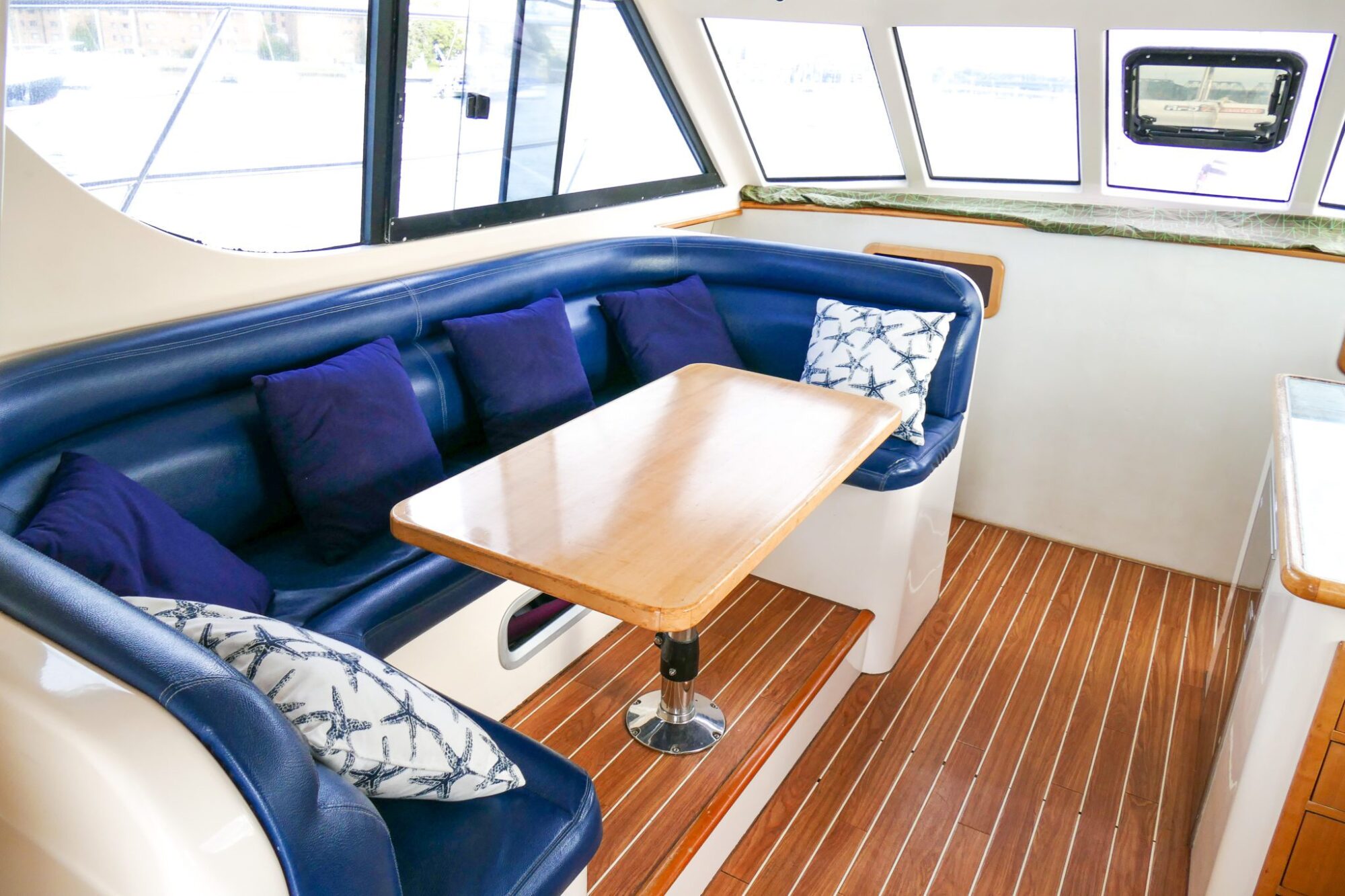 Experience a dining area inside a boat with a wooden table, blue cushioned seats, and several blue and white pillows. Perfect for corporate boat events in Sydney or private yacht charters around Sydney Harbour.