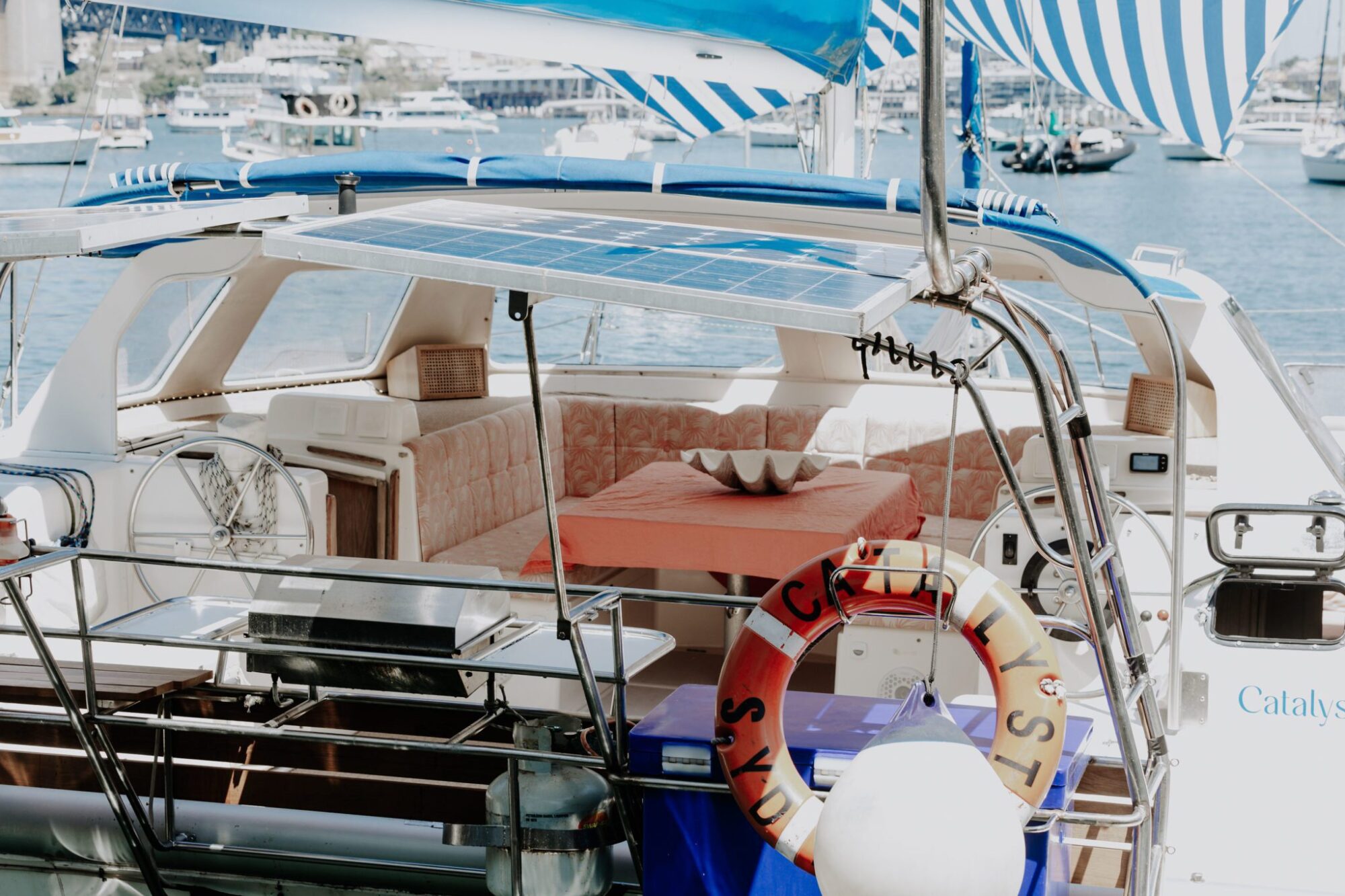 The deck of a docked sailboat with a shaded seating area, solar panels, a lifebuoy labeled "Catalyst," and various marine equipment and furnishings is perfect for corporate boat events Sydney or even a catamaran party Sydney.