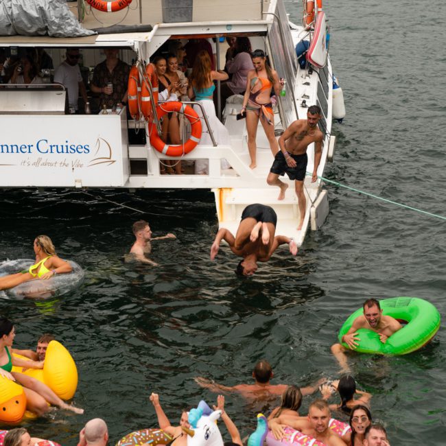 A group of people enjoying a Sydney boat party hire, some swimming and floating in the water with inflatables, while others are socializing on the luxurious yacht.