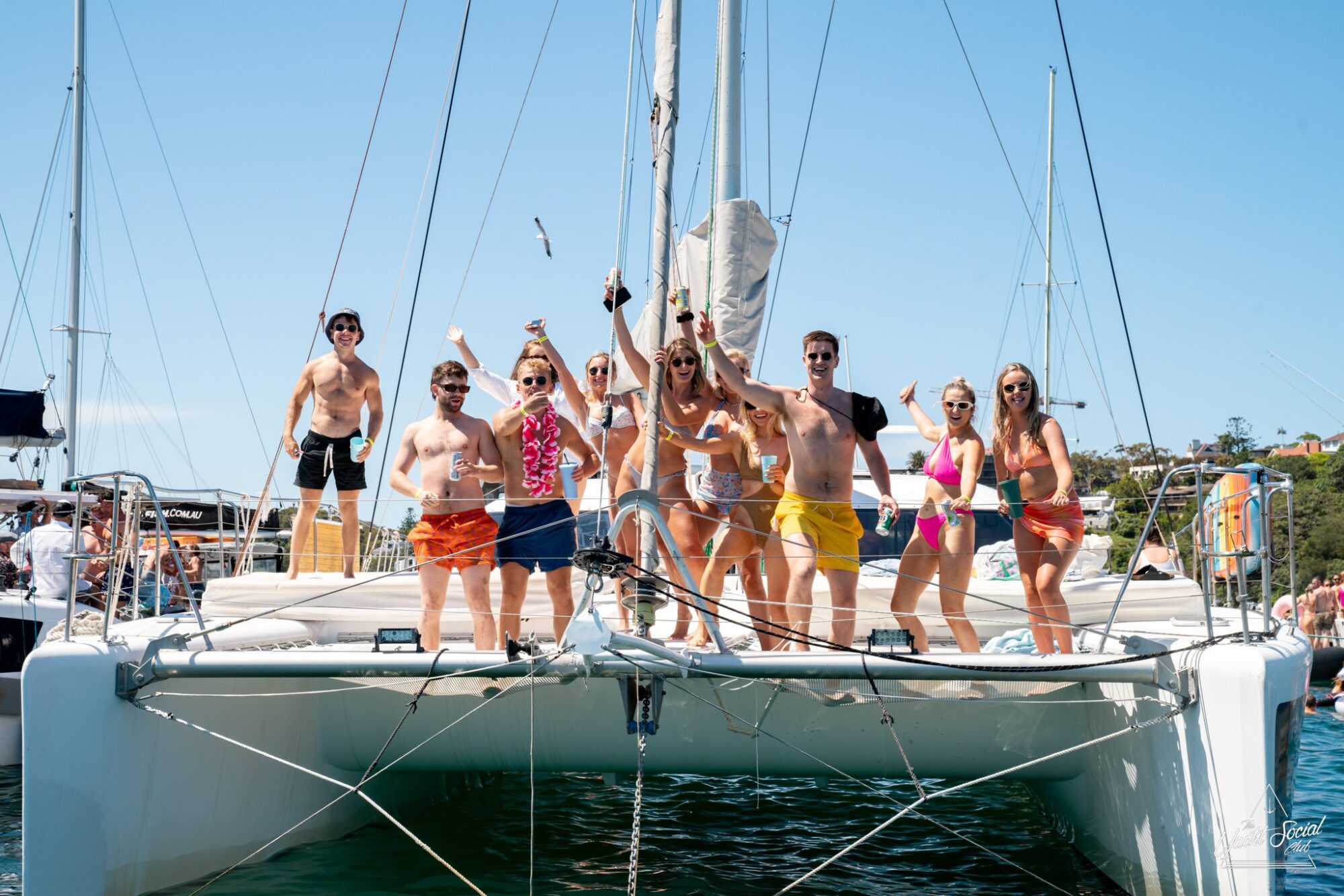 A group of people in swimsuits stand and pose on the deck of a luxury yacht hire Sydney in sunny weather.