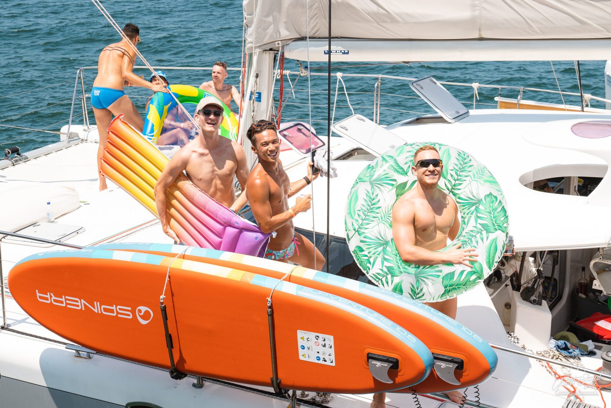 A group of four people wearing swimwear, holding colorful floats and a paddleboard, enjoying a luxurious yacht hire Sydney experience on a sunny day.