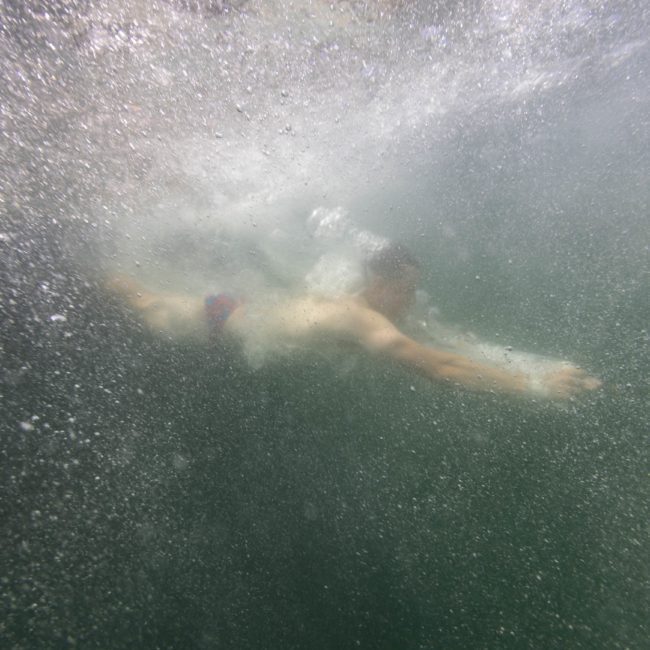 A person swimming underwater with outstretched arms, surrounded by bubbles and water currents, enjoying the tranquility reminiscent of a Sydney boat party hire.
