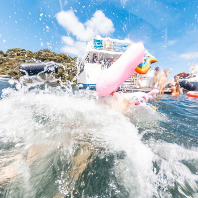 Person falling into water with a splash amidst boats and inflatable toys on a sunny day during a Sydney boat party hire.