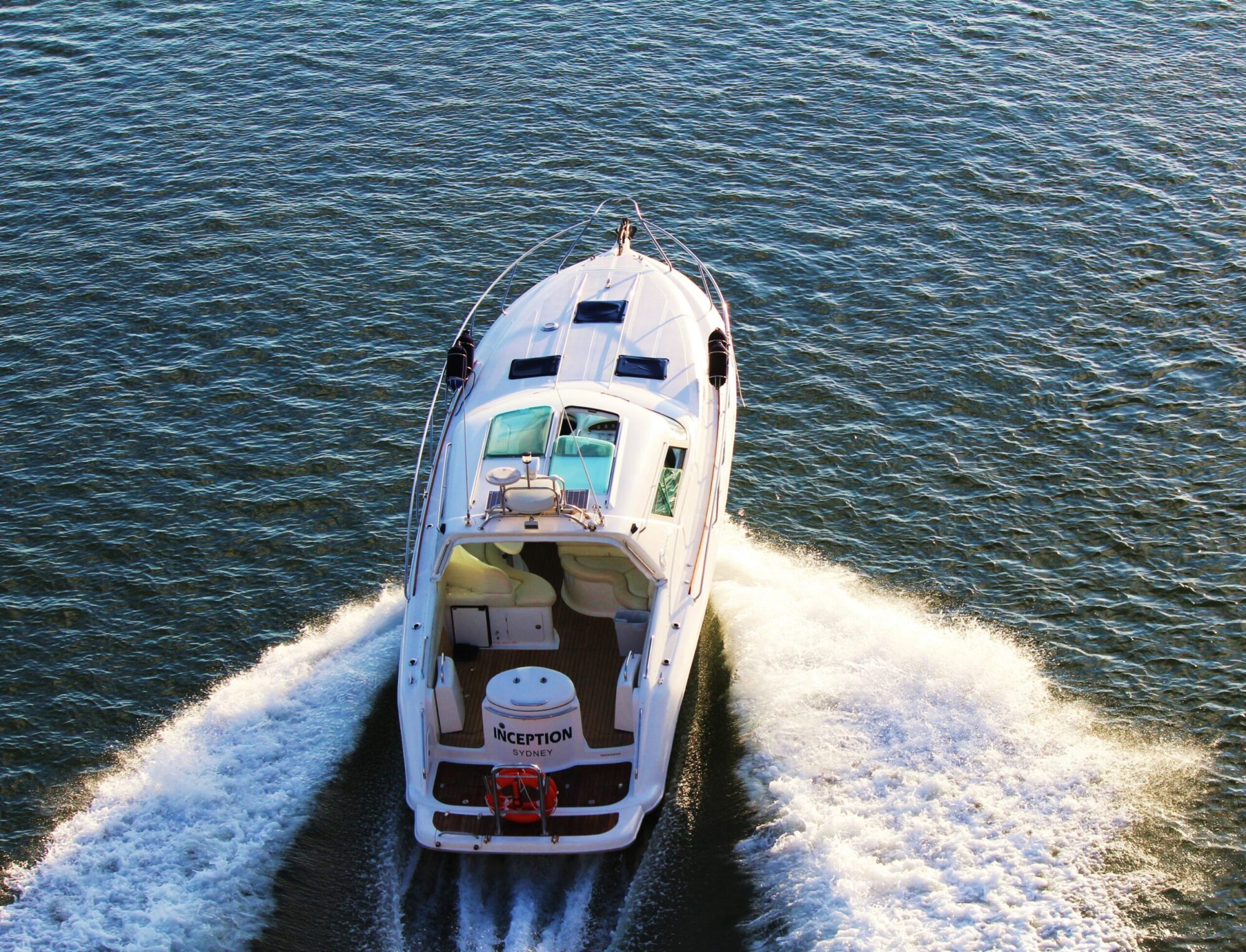 A white motorboat named "INCEPTION" cruises on a calm, reflective body of water, leaving a trail of foamy waves behind it. The boat features multiple windows and an open deck area, perfect for parties with The Yacht Social Club Event Boat Charters in Sydney.