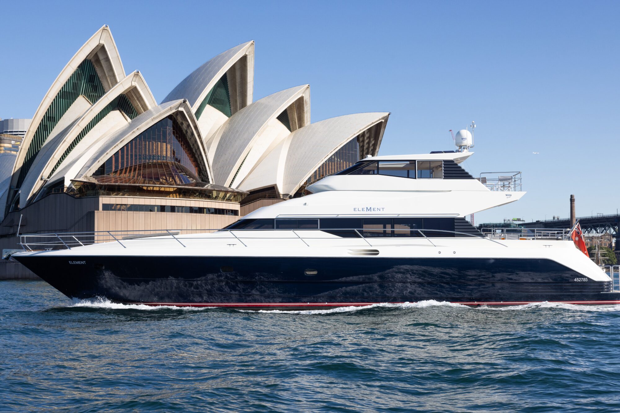 A luxury yacht sails on blue water in front of the Sydney Opera House under a clear sky.
