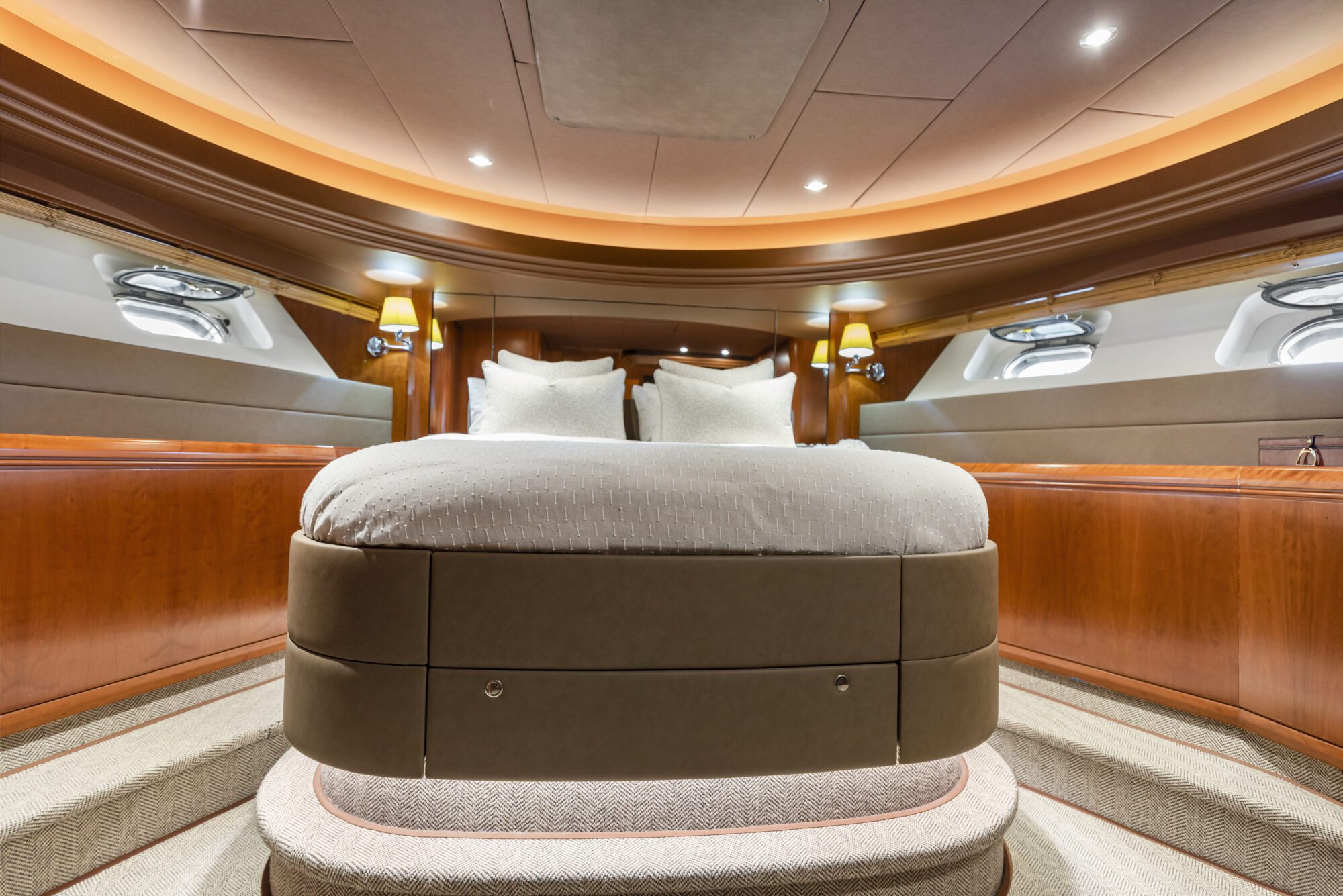 A luxurious yacht bedroom with a large, neatly made bed, wooden walls, ambient lighting, and small windows on both sides. The space has modern decor and a cozy, inviting atmosphere.