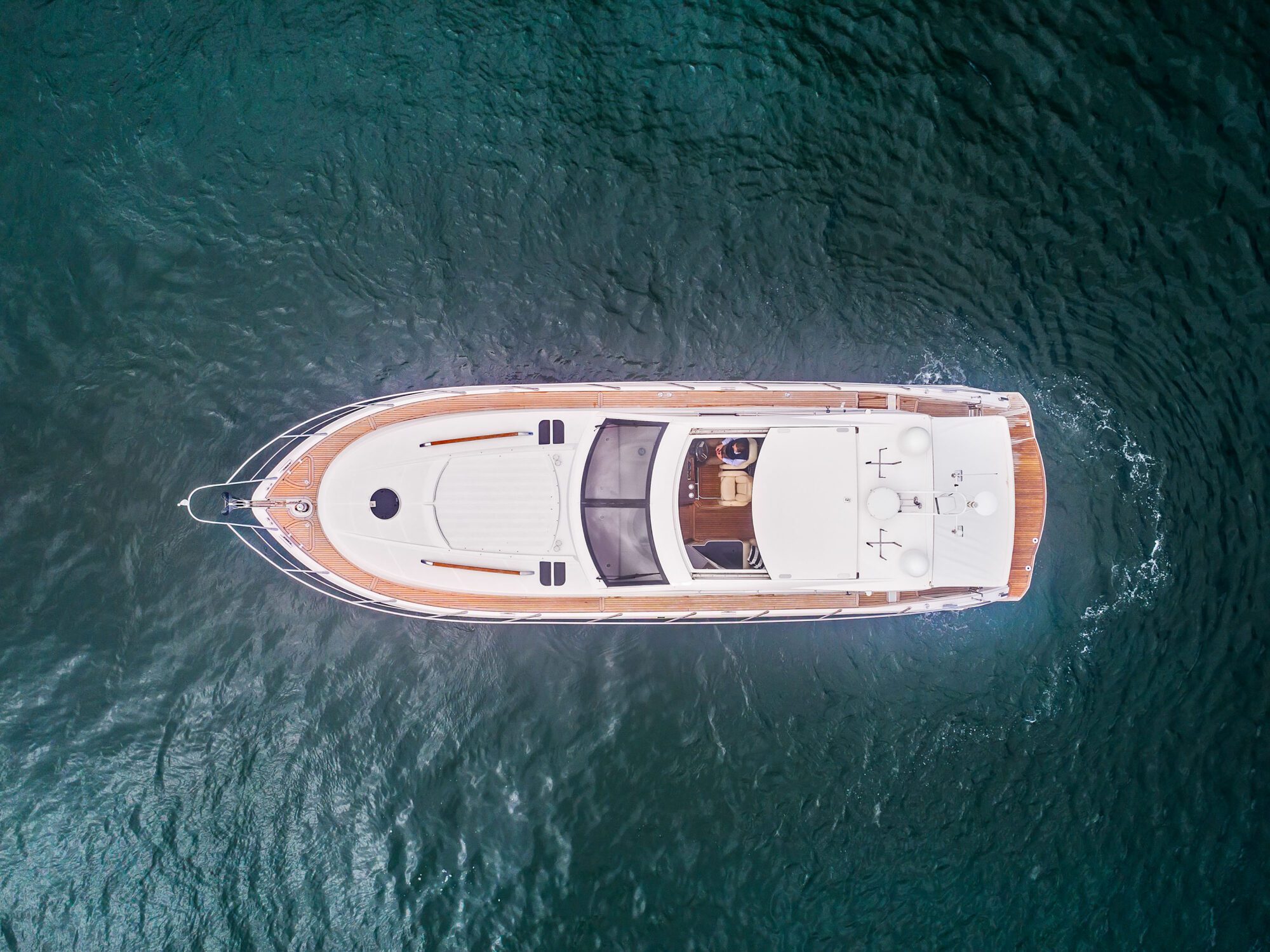 Aerial view of Birchgrove, a white luxury yacht, cruising on calm dark blue water, showcasing its deck, seating area, and rooftop details.