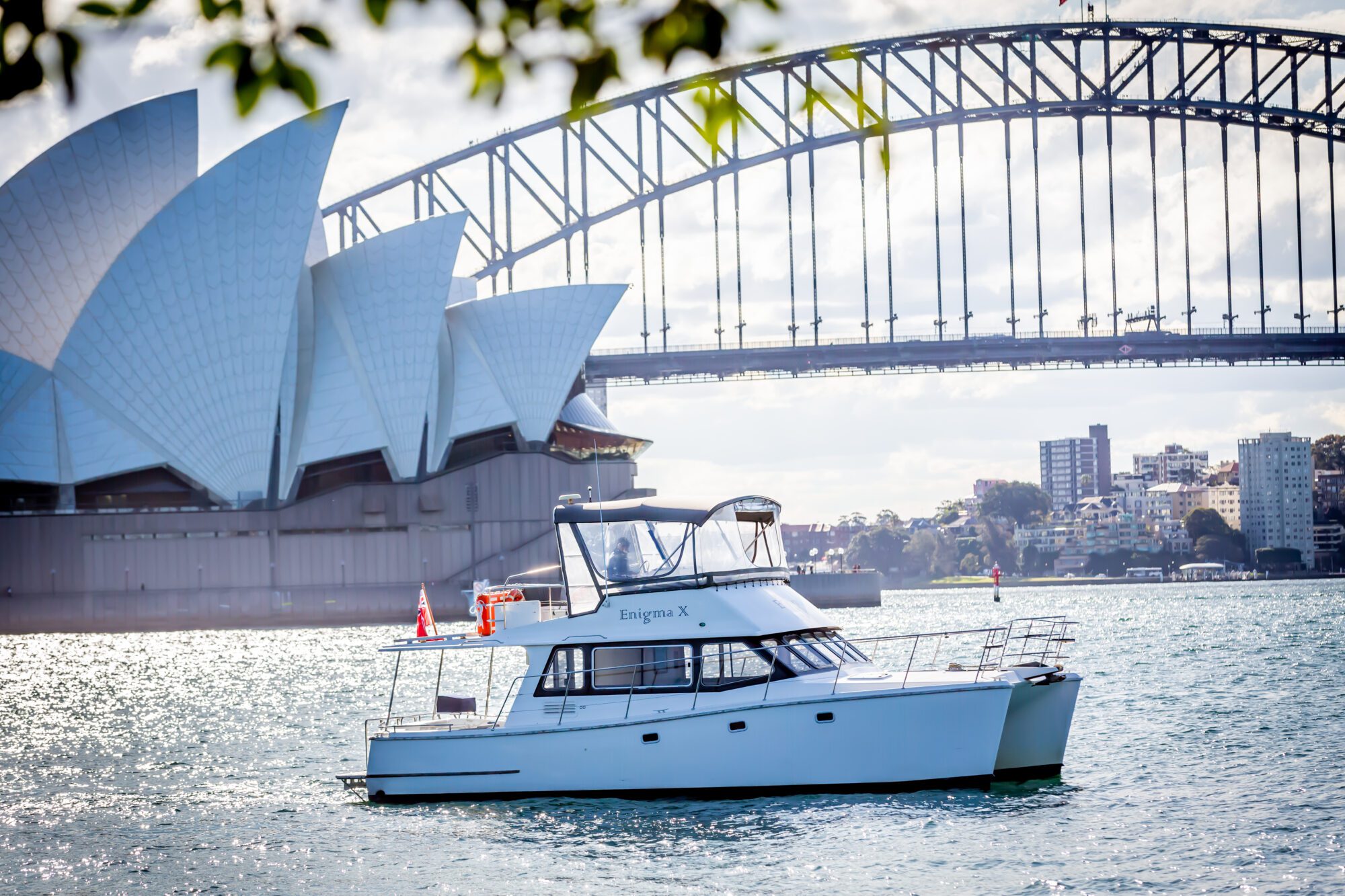A white boat floats on Sydney Harbour with the Sydney Opera House and Harbour Bridge in the background on a sunny day.