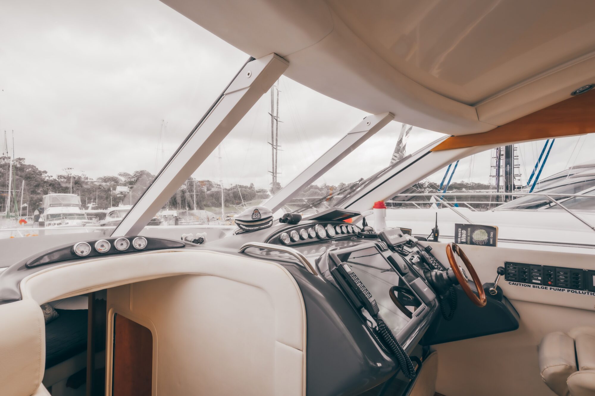 The interior cockpit of Coco, a modern yacht, features a steering wheel, control panels, navigation instruments, and large windows overlooking a marina with boats and masts visible outside.