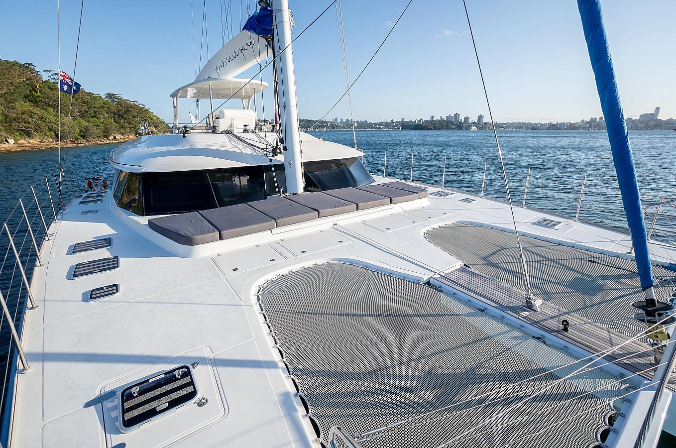 Enjoy the view from SV Feng's deck as you relax on sun loungers or the netted lounge, overlooking calm waters and a city skyline, with tree-lined shores to the left.